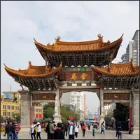 Traditional Chinese gate marking an entrance to downtown Kunming, with pedestrians walking beneath it.